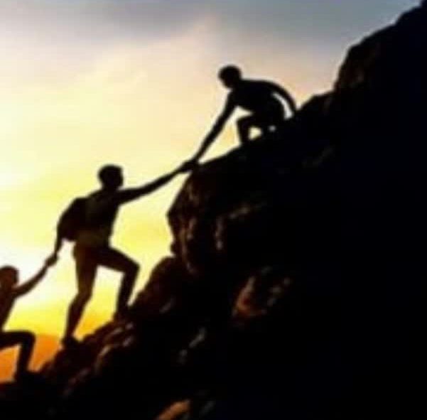 Climbers helping each other up a mountain at sunset