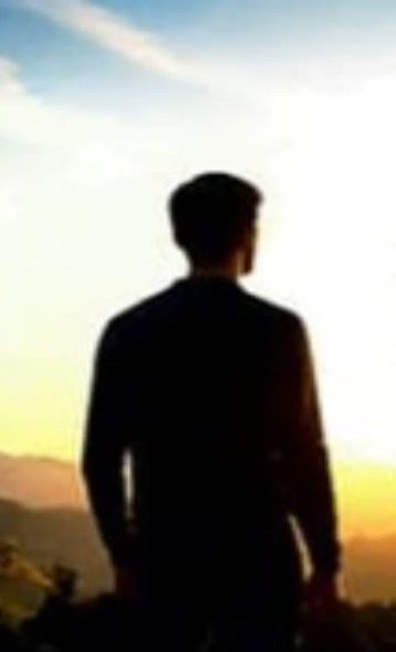 A person looking towards a golden sunrise over mountains